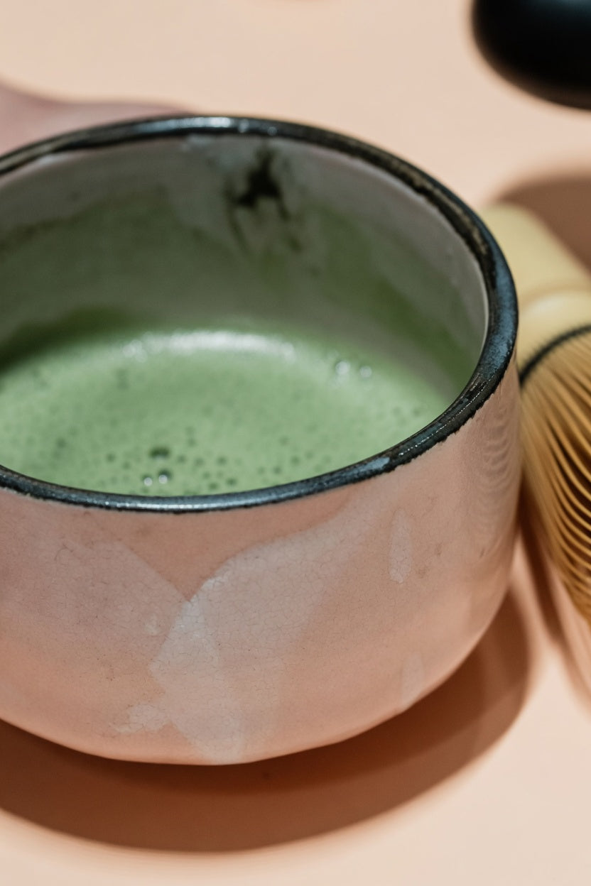 Handmade ceramic tea bowl with matcha foam and a bamboo whisk.