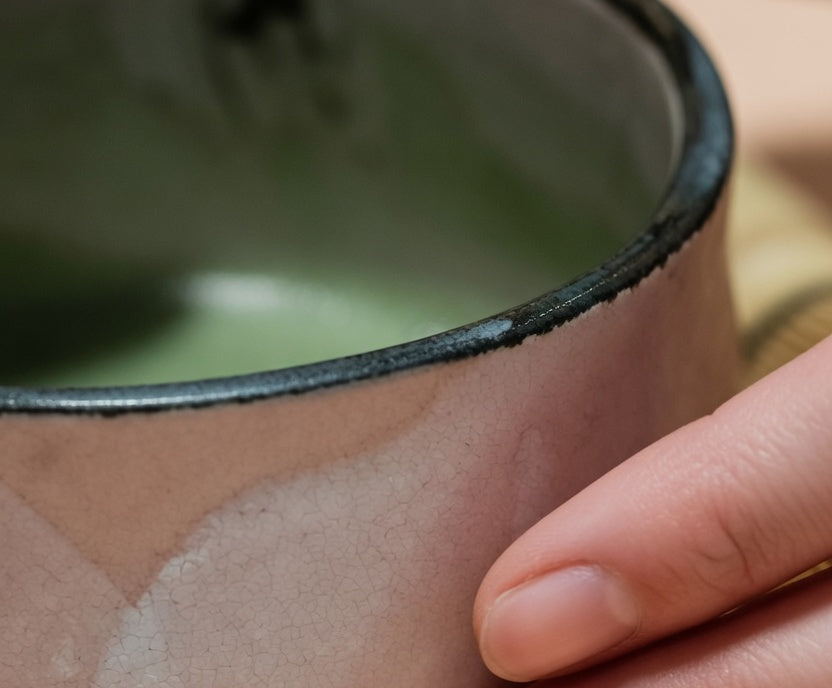 Fingers resting on the irregular glaze of a handmade bowl.